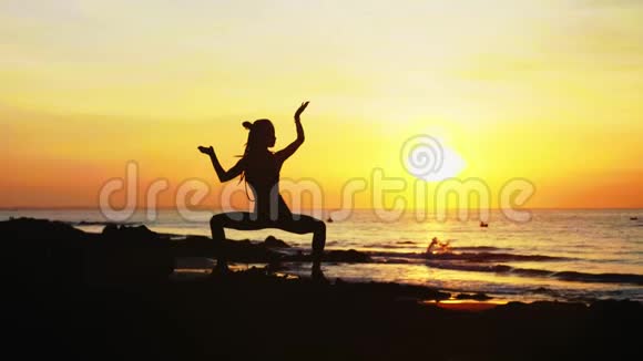 年轻女子她的剪影正在日落时在海边做瑜伽练习视频的预览图