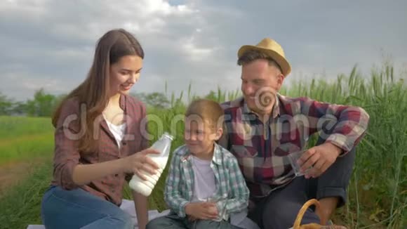 一家人闲着快乐的女人在户外野餐时把牛奶倒进杯子里送给小男孩和戴着帽子的微笑的男人视频的预览图