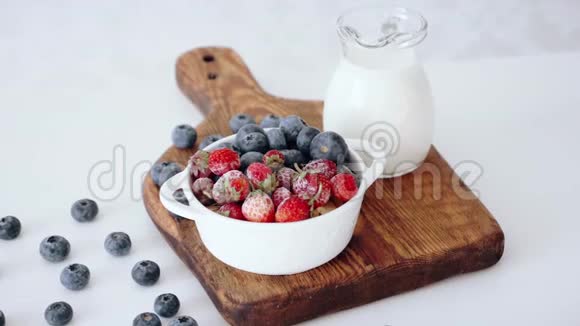 用草莓和蓝莓做成的碗放在带有牛奶的木切割板上视频的预览图