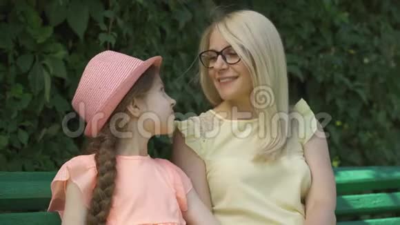成熟的金发母亲戴着眼镜小女儿坐在夏季公园的长凳上看着摄像机视频的预览图