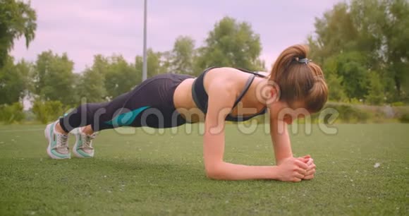 年轻的白种人运动健身女孩站在城市户外公园的木板上的特写照片视频的预览图
