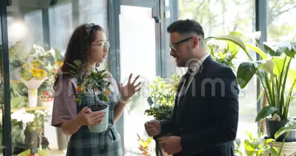 男性顾客与微笑的花店老板交谈讨论鲜花店里的异国植物视频的预览图