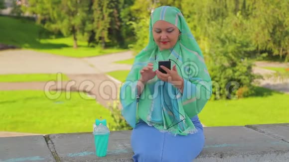 公园里一个戴着绿色围巾的年轻穆斯林女人喝咖啡在送信员里视频的预览图