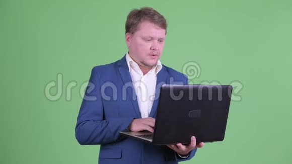 快乐超重长胡子的商人在用笔记本电脑说话视频的预览图