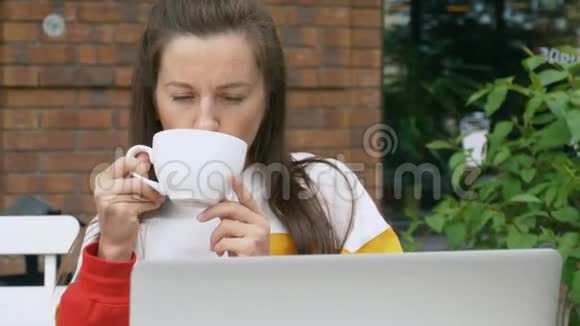 女人一边喝咖啡一边看着笔记本电脑视频的预览图