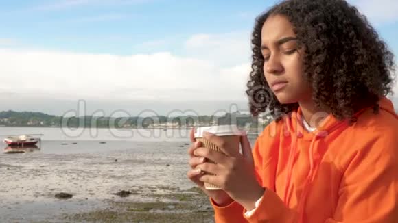 美丽的混血非裔美国少女在海边喝咖啡看上去悲伤或体贴视频的预览图