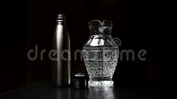 特写年轻的男性手倒水与玻璃壶在可重复使用钢热生态瓶在黑色工作室背景视频的预览图