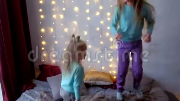 两个女孩姐妹在卧室里跳着床在圣诞节的室内有花环视频的预览图