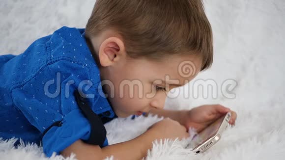 快乐的孩子很乐意用智能手机玩游戏躺在白色沙发上视频的预览图