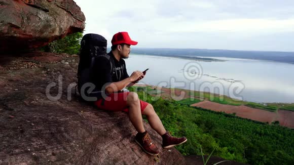 徒步旅行者坐在悬崖边的岩石山顶上用智能手机视频的预览图