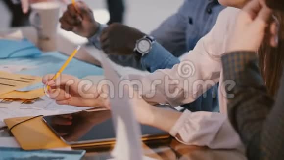 特写忙碌的各种商务人士坐在大办公桌后面与设备和文件合作开会视频的预览图