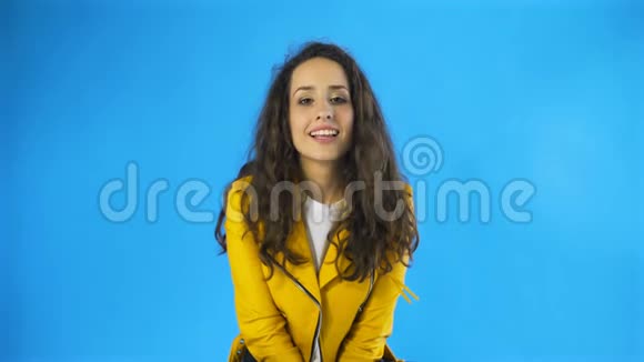 穿着黄色夹克的快乐漂亮女人在蓝底工作室眨眼视频的预览图