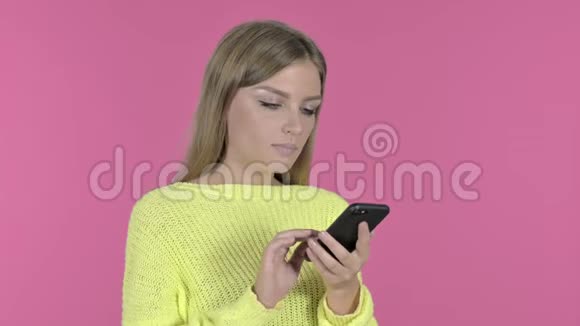 在使用智能手机时兴奋的女孩作弊成功粉红背景视频的预览图