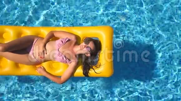 在游泳池里的黄色充气床垫上可以看到美丽的晒黑女孩戴着太阳镜和粉红色比基尼视频的预览图