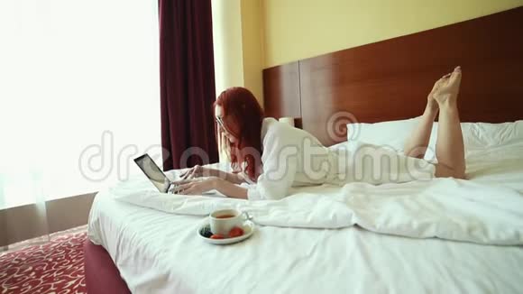 一个生姜女人躺在床上拿着笔记本电脑工作喝茶视频的预览图