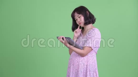 快乐的亚洲孕妇用数码平板电脑思考视频的预览图