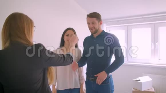 女房地产经纪人把新家的钥匙交给快乐的年轻兴奋的夫妇并与他们握手视频的预览图