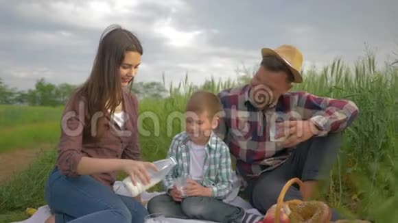 带着丈夫和小男孩微笑的妻子在家庭野餐时把牛奶倒进杯子里喝酒视频的预览图