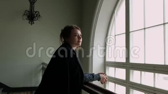 一个穿着黑色外套的中年黑发女人正靠在栏杆上靠在一大窗户上视频的预览图