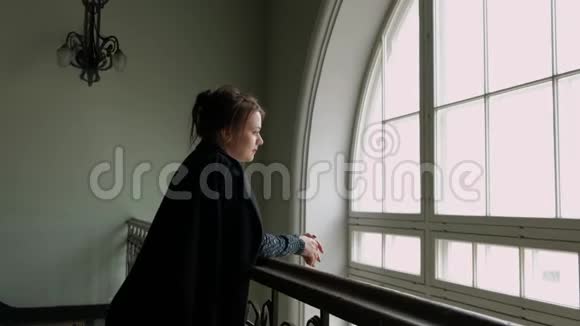 一个穿着黑色外套的中年黑发女人正靠在栏杆上靠在一大窗户上视频的预览图