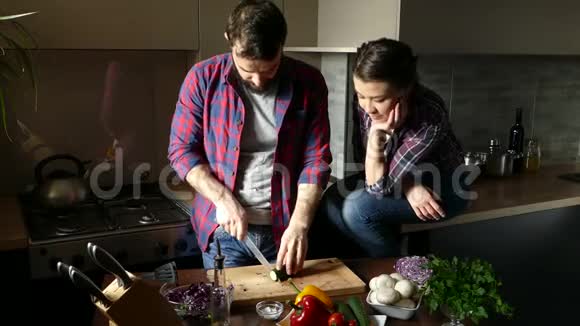 一对年轻漂亮的夫妇在家厨房边煮健康食品男人切沙拉给女人一点黄瓜的味道S公司视频的预览图