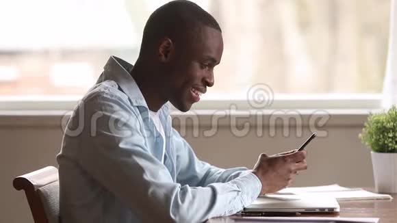 微笑的非裔美国人拿着智能手机使用应用程序短信视频的预览图