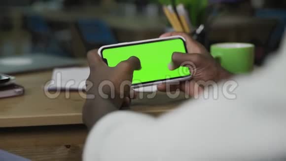 非裔美国人手在带有绿色屏幕的水平智能手机上滚动网页视频的预览图