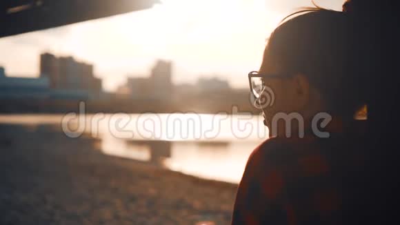 漂亮的年轻女孩戴着眼镜穿着红色格子衬衫放松一下背景是海滩日落的城市景观视频的预览图