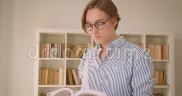 一位年轻成功的高加索男学生戴着眼镜看着图书馆里的照相机看书的特写肖像视频的预览图