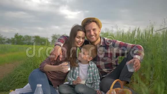 一家人的闲情逸致微笑的妈妈和爸爸和儿子拥抱在大自然的绿野野炊中放松视频的预览图