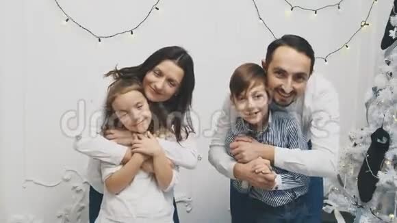 幸福的家庭成员母亲抱女儿父亲抱儿子在圣诞树附近的白色背景上视频的预览图
