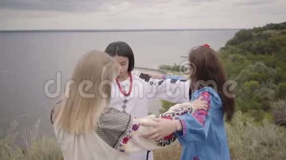 三个漂亮的女朋友穿着夏天的长时装在田野上背景是湖或河二视频的预览图