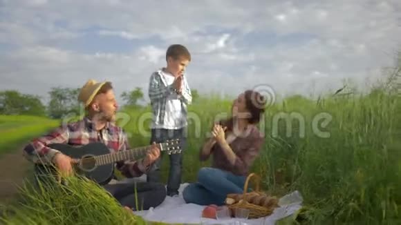 有趣的家庭快乐的男性弹吉他而女性带着孩子跳舞和鼓掌同时放松家庭野餐自然视频的预览图