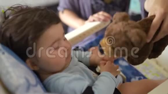 母亲在孩子座位上和熊玩她的小儿子亚洲混血儿穿蓝色体恤的男孩视频的预览图