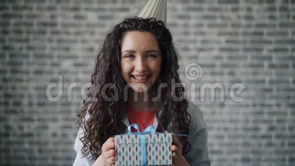 戴着派对礼帽的可爱女孩的肖像礼物盒微笑着看着镜头视频的预览图