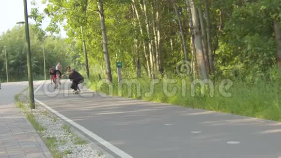 三个年轻人在被森林包围的绿色公园的路上玩滑板视频的预览图