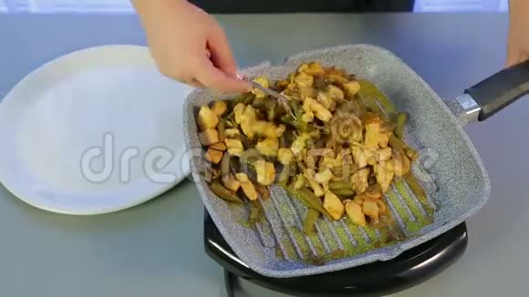 一个女人把带着绿豆和蘑菇的炸鸡从煎锅里移到一个白色的盘子里时间跨度视频的预览图