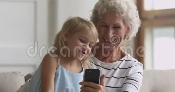 快乐的老奶奶和孙子在家用智能手机视频的预览图
