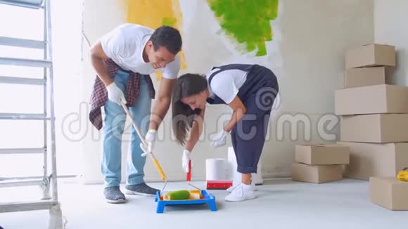 家庭装修年轻的幸福夫妇用油漆滚筒粉刷他们的新房子内部视频的预览图