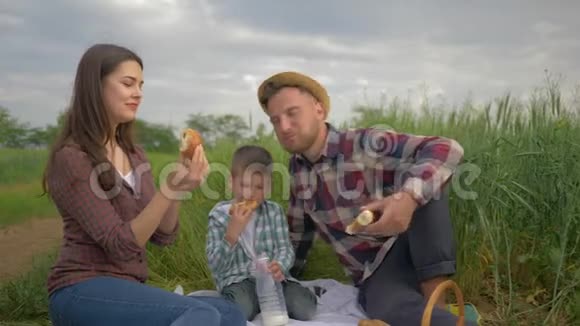 野餐快乐的女性喂养包子男人的小面包在户外绿色家庭野餐时小男孩喝牛奶的人一起放松视频的预览图