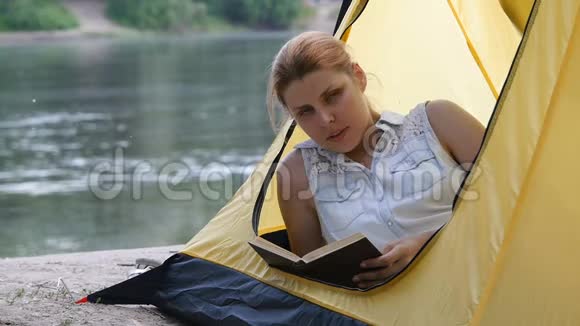 年轻的远足女孩在露营帐篷里看书做梦环顾四周开心的微笑健康活跃的生活方式理念视频的预览图