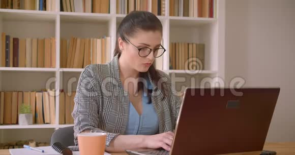 一位年轻成功的高加索女商人戴着眼镜用手提电脑在图书馆庆祝的特写镜头视频的预览图