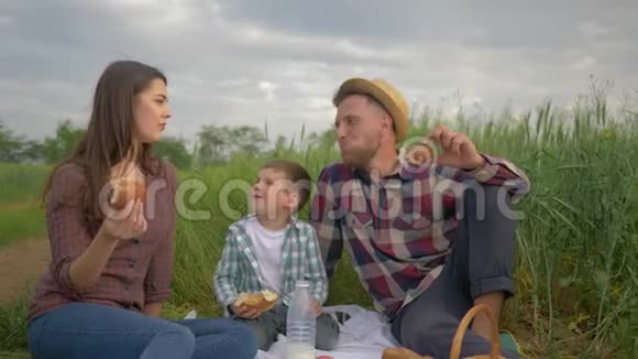 在大自然中休息一家人和一个孩子聊天在户外绿色的田野和天空野餐时吃面包店视频的预览图