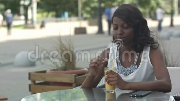 非洲年轻女子一边喝橙汁一边在咖啡馆里做梦的肖像视频的预览图