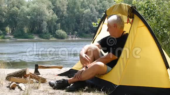 年长老人远足者50多岁坐在帐篷里露营者喝咖啡或茶河流和森林视频的预览图