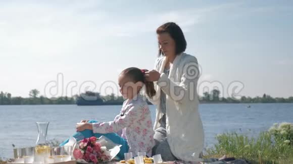 母亲照顾幸福的妈妈做女儿辫子休息期间在附近的家庭野餐视频的预览图