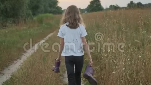小女孩手里拿着靴子走在乡间的路上视频的预览图