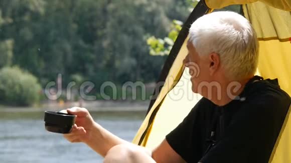 活跃的老年观念年长的男性徒步旅行者坐在帐篷里喝茶或咖啡可爱的白发男人关门视频的预览图
