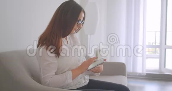 特写侧景照片年轻的白种人妇女戴着眼镜使用平板电脑并显示绿色的彩色屏幕以显示视频的预览图