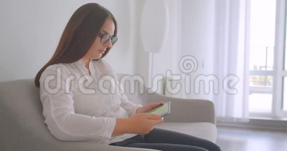 特写侧景照片年轻的白种人妇女戴着眼镜使用平板电脑并显示绿色屏幕拍摄坐姿视频的预览图